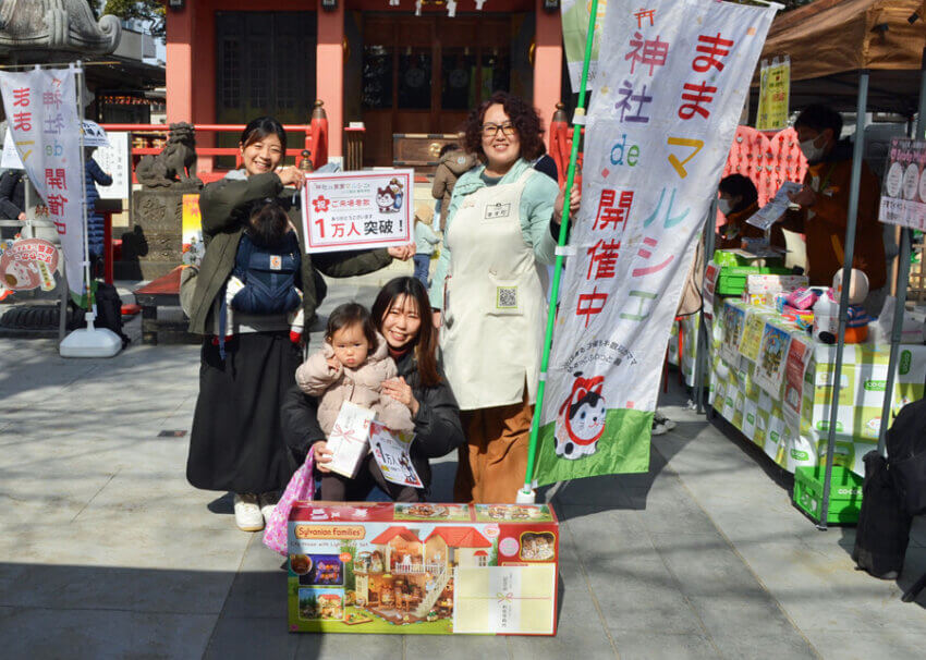 「神社ｄｅままマルシェ」で実行委員会（後列右は増田さん）
から記念品が贈られた、来場者１万人目の親子（前列）