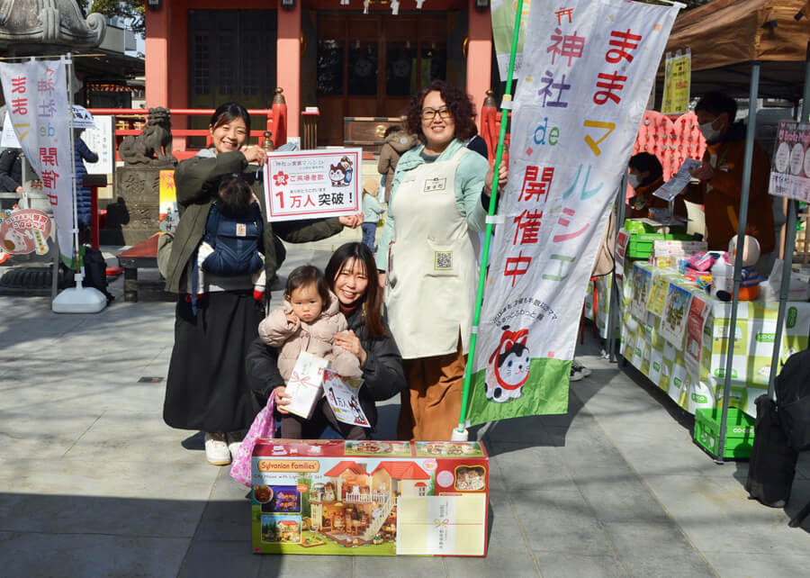 「神社ｄｅままマルシェ」で実行委員会（後列右は増田さん） から記念品が贈られた、来場者１万人目の親子（前列）