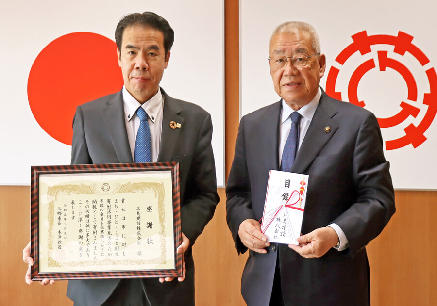 贈呈式で木津市長（右）に寄付金100万円の目録を手渡し、感謝状を受け取る広島建設の島田社長