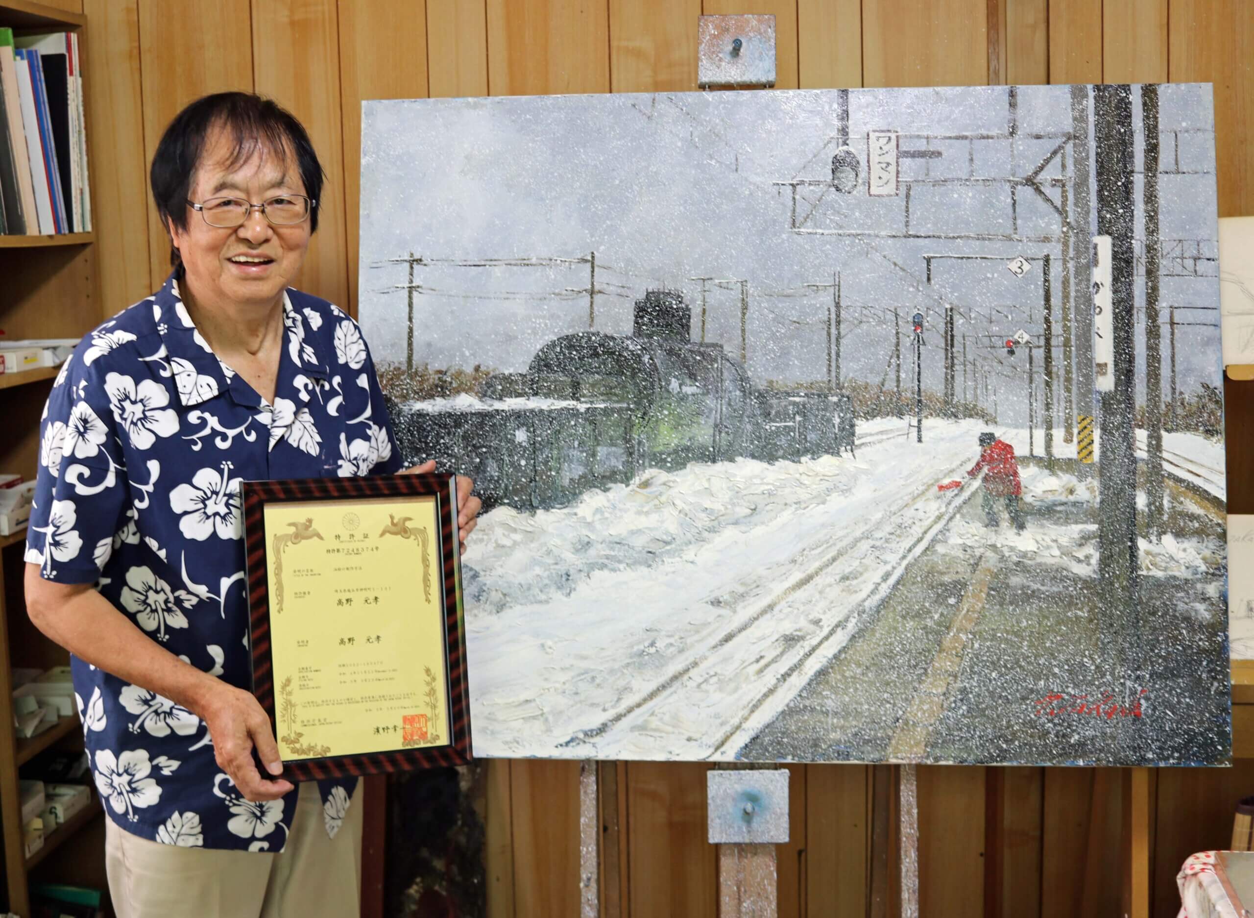 作品の前で特許証を手にする高野画伯